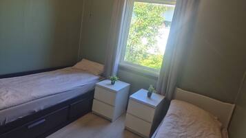 Ein Schlafzimmer mit zwei Betten, einem Fenster mit Vorhängen und Nachttischen mit Pflanzen.