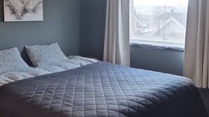 Un dormitorio con cama, una lámpara en el techo, una ventana con cortinas y una obra de arte colgada en la pared.