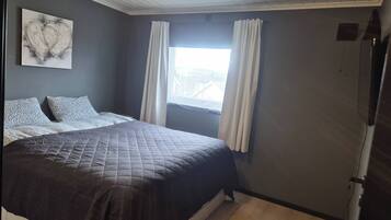 A bedroom with a bed, curtains, a window, and a wall-mounted artwork.
