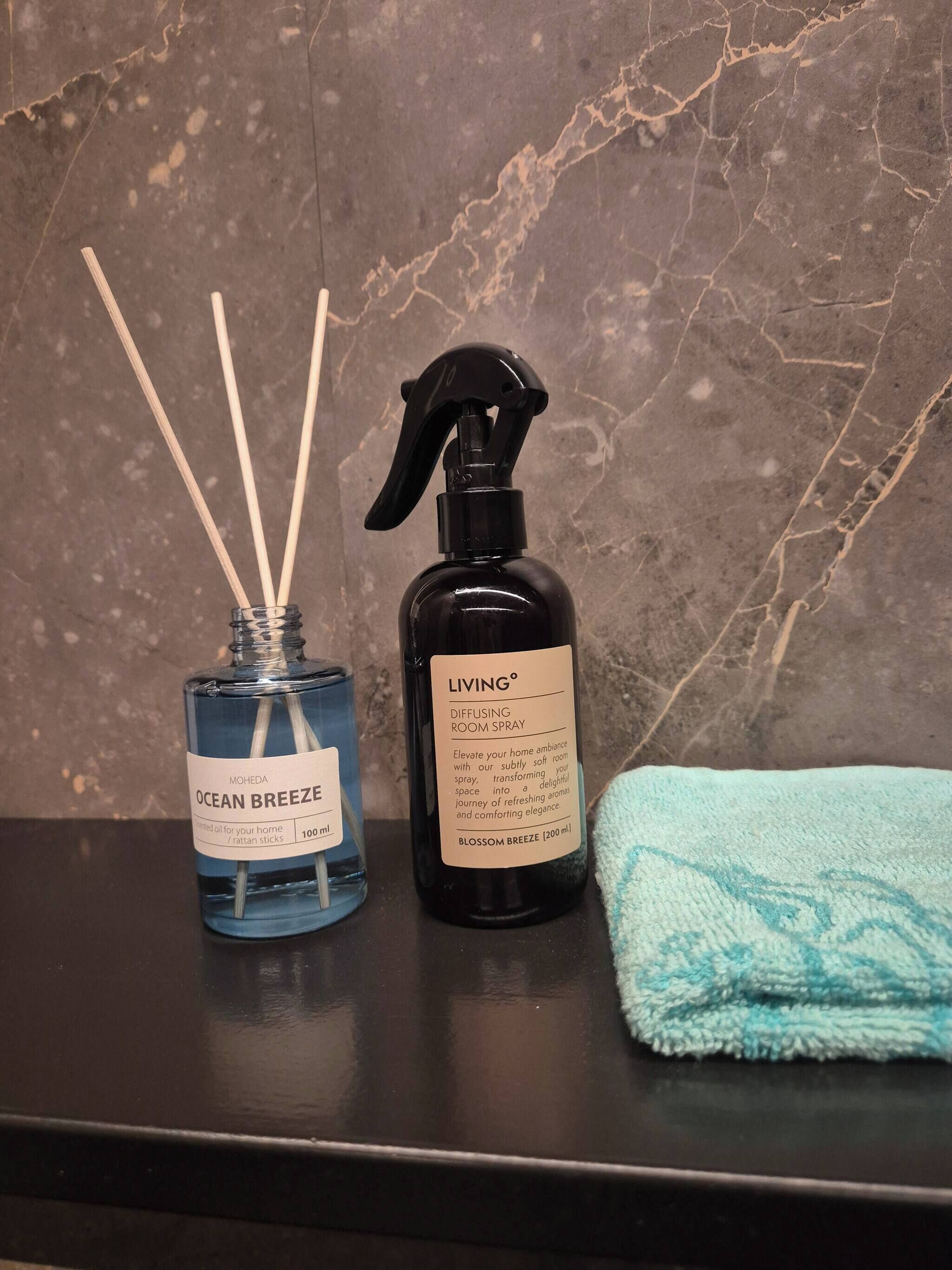 Two bottles of room spray and reed diffusers on a dark countertop with a marble background.
