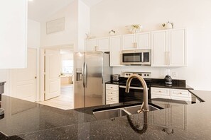 A modern kitchen with white cabinetry, stainless steel appliances, a black granite countertop, and a stainless steel sink. - Newly Listed - Briarwood Pool/Spa home w/outdoor 65" smart TV & conversational seating area (Naples)