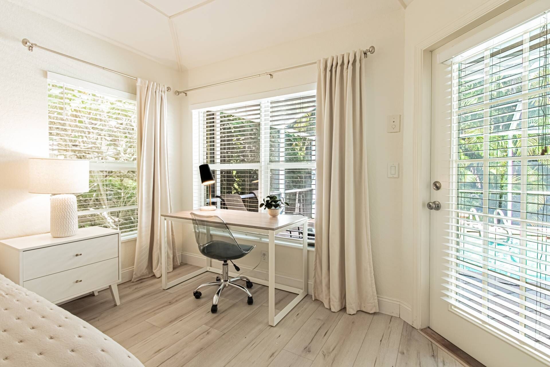 Un dormitorio con cama, un escritorio con silla, una lámpara y una ventana con cortinas.
