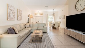 Ein Wohnzimmer mit Ecksofa, Couchtisch, Fernseher und einem Essbereich mit Stühlen und Tisch.