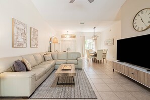 Ein Wohnzimmer mit Ecksofa, Couchtisch, Fernseher und einem Essbereich mit Stühlen und Tisch.