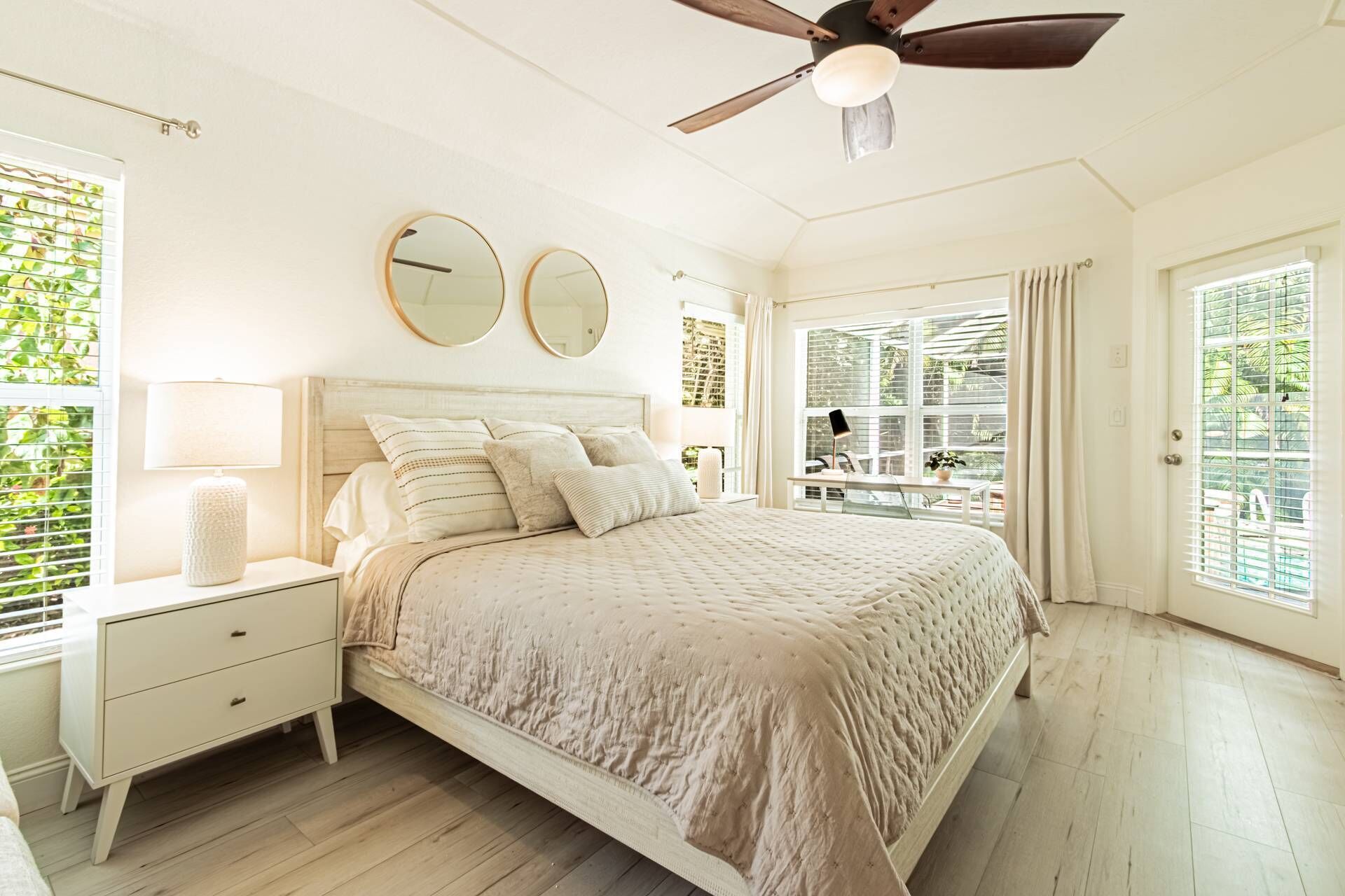 A bedroom with a bed, bedside tables, a ceiling fan, and large windows.