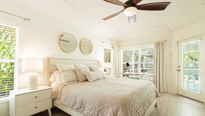Ein Schlafzimmer mit Bett, Nachttischen, Deckenventilator und großen Fenstern.