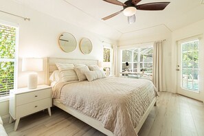 Ein Schlafzimmer mit Bett, Nachttischen, Deckenventilator und großen Fenstern.