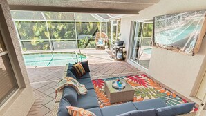 Eine sonnendurchflutete Terrasse mit Pool, einer gepolsterten Sitzgruppe und einem Grill.