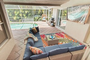 Eine sonnendurchflutete Terrasse mit Pool, einer gepolsterten Sitzgruppe und einem Grill.
