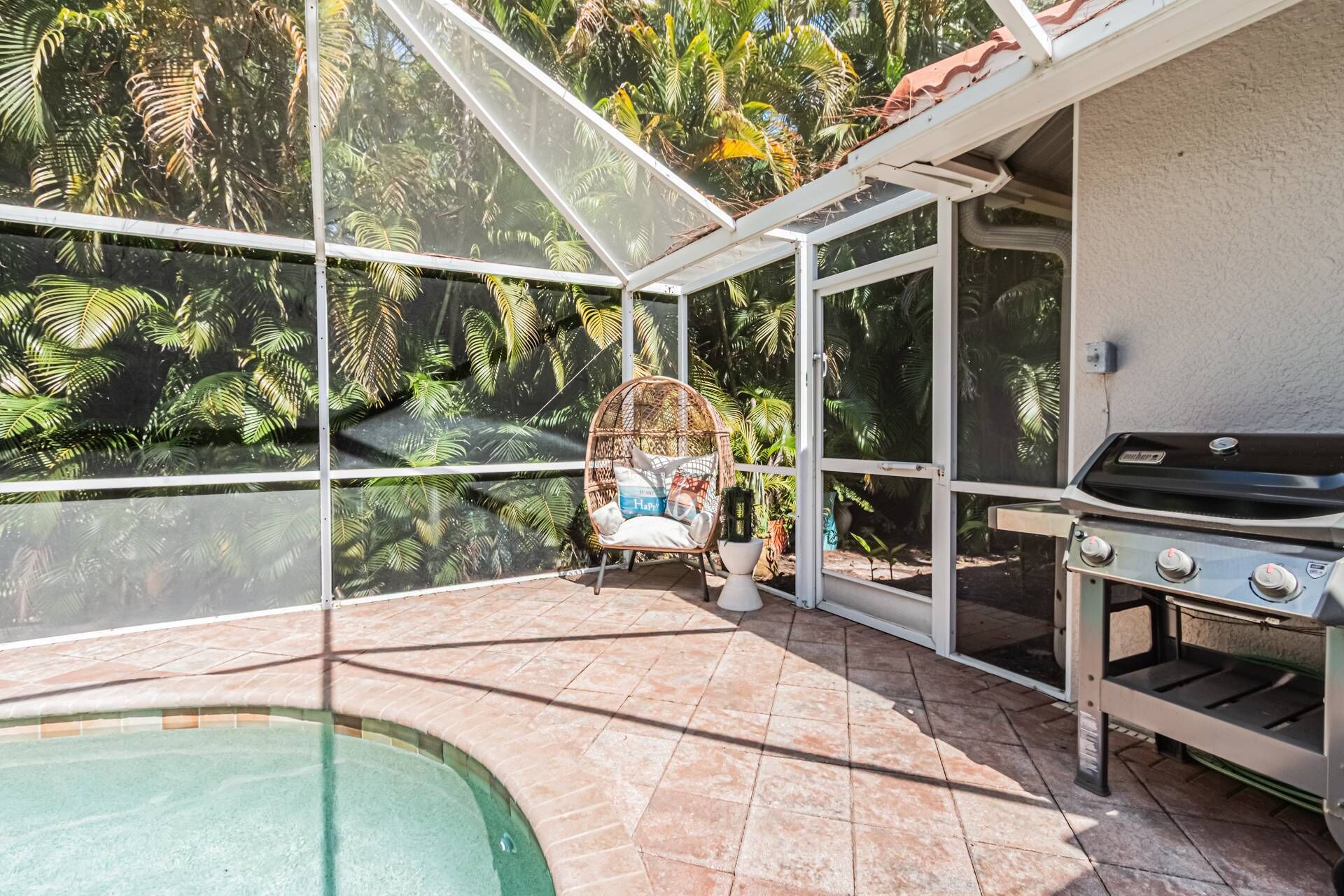 Un solárium con cerramiento de vidrio, piscina, parrilla y una silla de mimbre.