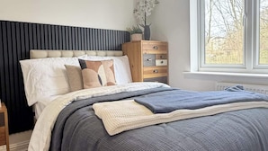 A bedroom with a bed, bedside table, dresser, window, and a hanging light fixture. - Executive 2-bedroom Corporate Space In West Yorkshire, United Kingdom (Leeds)