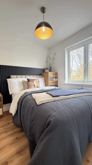 Ein Schlafzimmer mit Bett, Nachttisch, Kommode, Fenster und einer Pendelleuchte.