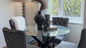 A dining area with a glass table, four upholstered chairs, a lamp, and a window with a view of trees. - Executive 2-bedroom Corporate Space In West Yorkshire, United Kingdom (Leeds)