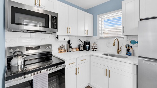 A modern kitchen with stainless steel appliances, white cabinetry, and a window with blinds.