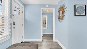 A hallway with a door, a bench, a wall-mounted mirror, and a framed picture.