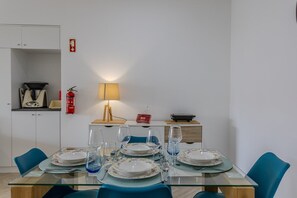 A dining area with a glass table set for four, blue chairs, a lamp, and a fire extinguisher on the wall. - GuestReady-Charming Retreat in Ribeira Grande (Ribeira Grande)