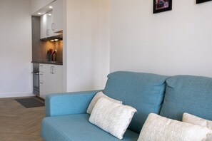 A living room with a teal sofa and white cushions, a kitchen in the background, and a framed picture on the wall. - GuestReady-Charming Retreat in Ribeira Grande (Ribeira Grande)