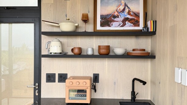 Une cuisine compacte dotée d’un four encastré, d’un évier et d’un mur en bois orné d’un tableau encadré.