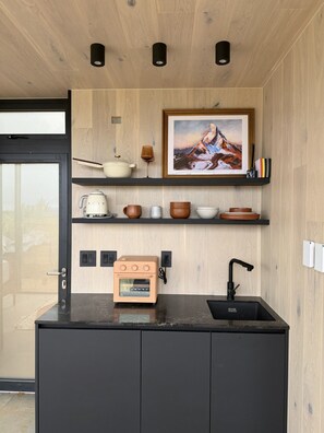 Cozinha compacta com forno embutido, pia e parede de madeira com um quadro emoldurado.