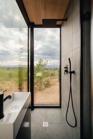 Ein modernes Badezimmer mit großem Fenster, einer Dusche und einem Waschbecken.