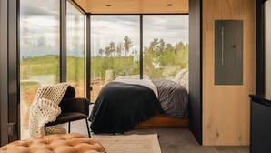 Une chambre avec une grande fenêtre, un lit, une chaise et un plafond en bois.