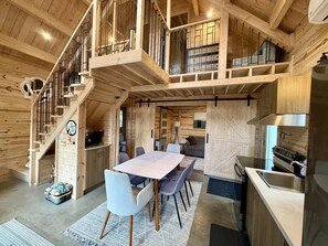 A wooden interior with a dining area, kitchen, and a staircase.