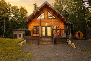 A wooden cabin with a front porch, a chimney, and a small attached shed.