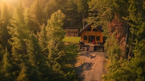 A cabin with a porch and a pathway leading to it, surrounded by dense forest. - Sauna, Spa & Nature | Le Kanouk (Lac-Etchemin)
