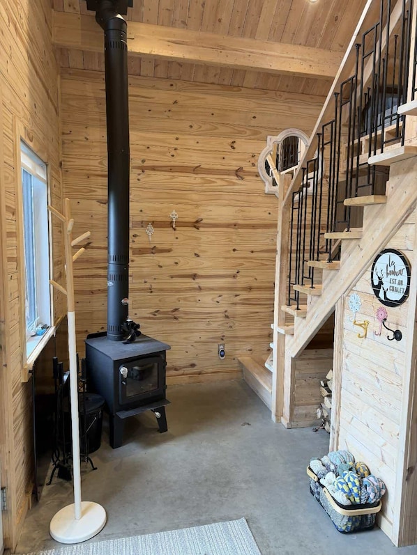 A wooden interior with a black wood stove, a staircase, and a window. - Sauna, Spa & Nature | Le Kanouk (Lac-Etchemin)