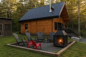 A log cabin with a fireplace, outdoor seating, and a metal roof. - Sauna, Spa & Nature | Le Kanouk (Lac-Etchemin)