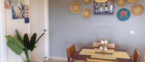 A dining area with a wooden table and chairs, a hanging light fixture, and decorative wall hangings.