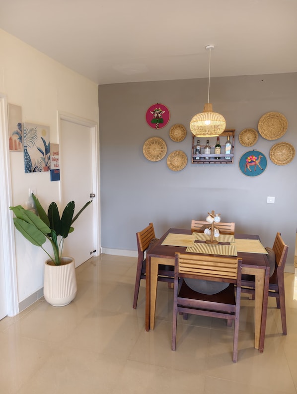 A dining area with a wooden table and chairs, a hanging light fixture, and decorative wall hangings.