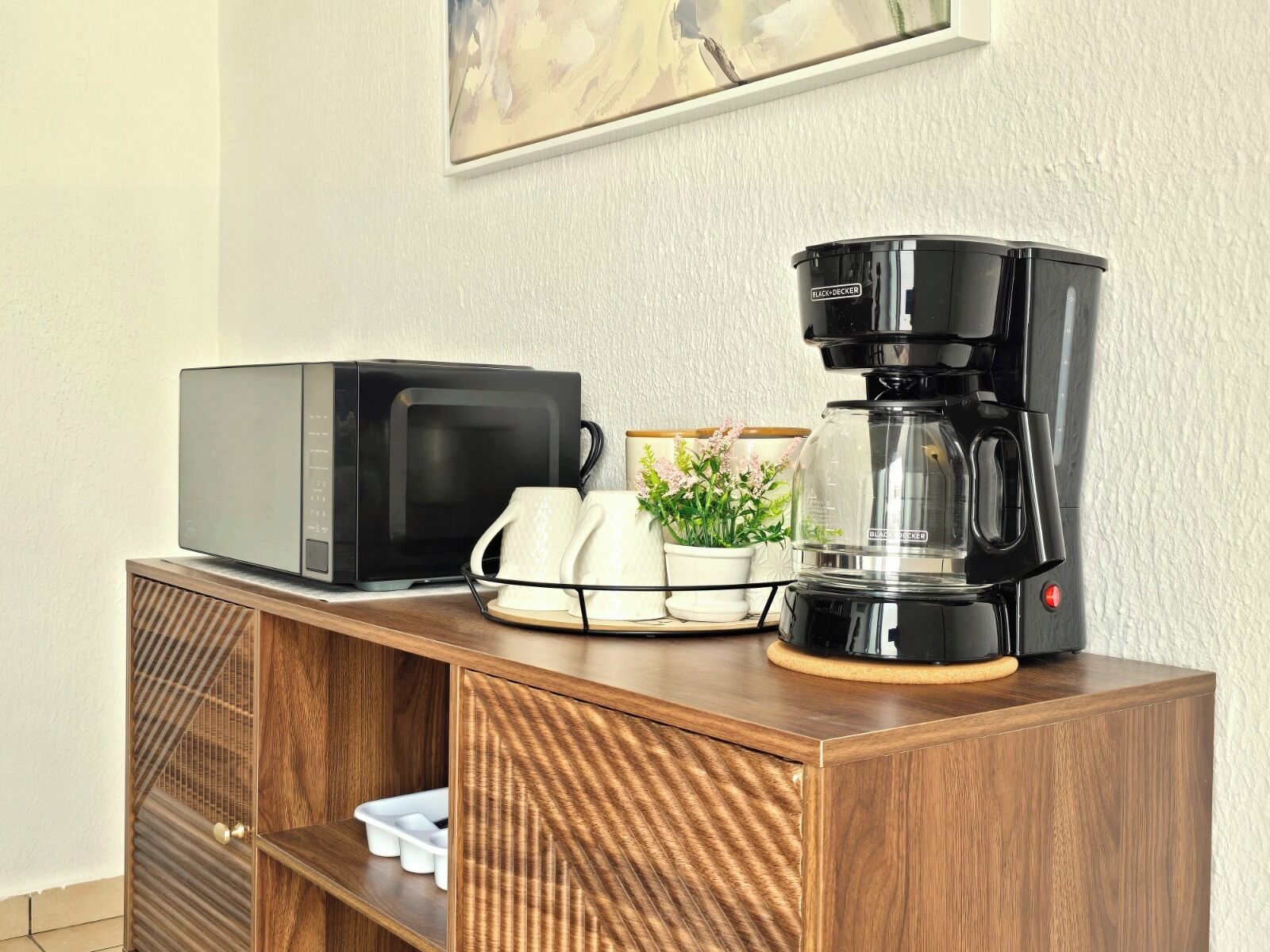 Micro-ondas, máquina de café e uma pequena planta em vaso sobre um armário de madeira.