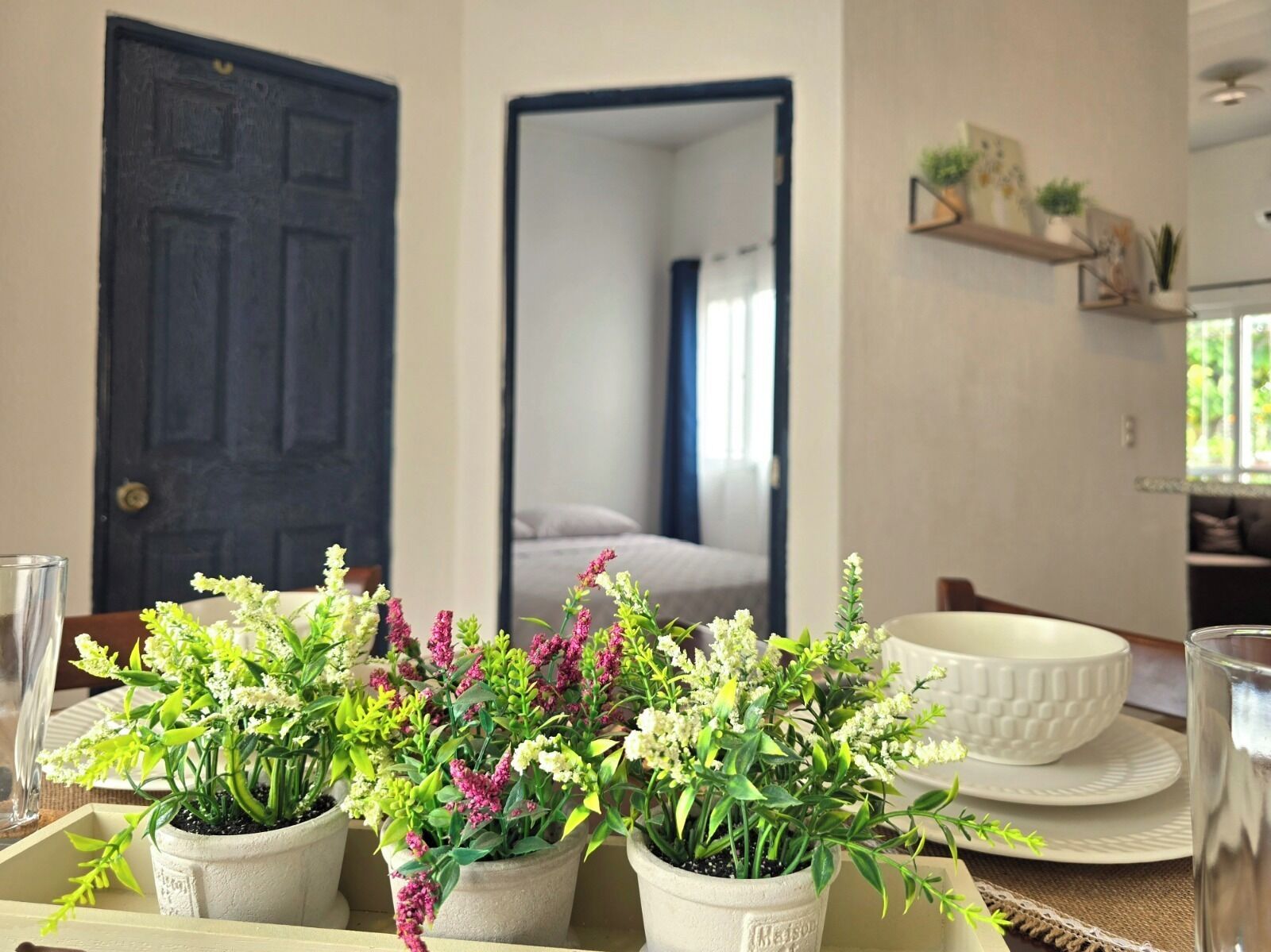 A dining area with a table set for two, potted plants, a white bowl, and a glass.