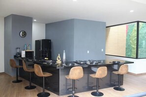 A modern kitchen with a central island, bar stools, a refrigerator, and a clock on the wall. - The Glass & Stones Oasis: An Urban Sanctuary (Temixco)