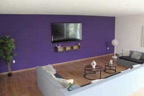 A living room with a flat-screen TV, a sofa, a coffee table, a fan, and a potted plant. - The Glass & Stones Oasis: An Urban Sanctuary (Temixco)