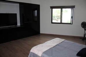 Un dormitorio con cama, televisión, ventana y ventilador.