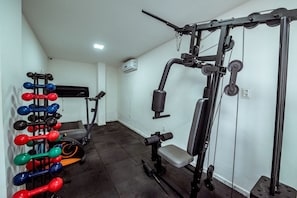Une salle de sport équipée de matériel de musculation, d’un banc et d’un tapis de course.
