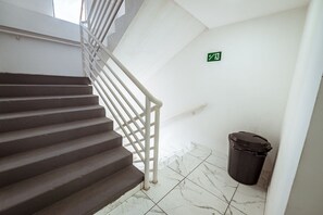 A staircase with a white railing, a trash bin, and a green emergency exit sign. - Apto com Piscina Academia e Churrasqueira (João Pessoa)