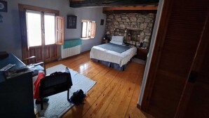 A bedroom with a stone fireplace, wooden beams, a bed, and a desk with a chair. - Casa Los Josuco, located in the heart of the Saja-Besaya Natural Park. (Collado de Cieza)