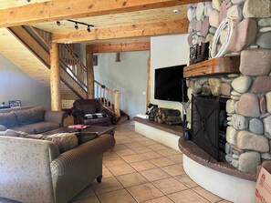 Un salon avec une cheminée en pierre, un téléviseur et un escalier.