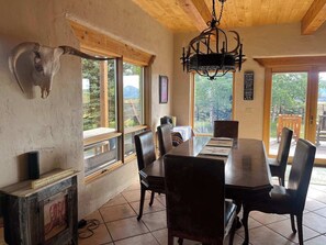Ein Essbereich mit Holztisch und Stühlen, großen Fenstern mit Bergblick, einer Chandelierleuchtre und einem aufgehängten Tierkopf an der Wand.