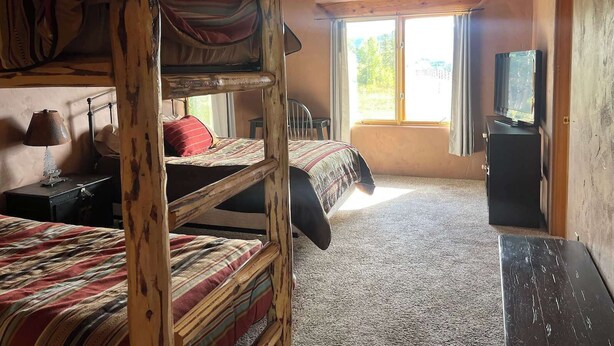 A room with bunk beds, a desk, a lamp, a television, and a window with curtains. - Studley Ranch-Private hot tub and pet friendly (Crested Butte)