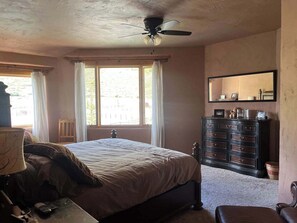 Une chambre à coucher avec un lit, une commode, un ventilateur de plafond et une fenêtre avec des rideaux.