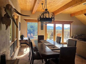 Un espace repas avec une longue table, des chaises et un lustre. Une grande fenêtre offre une vue sur l’extérieur.