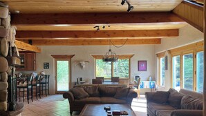A spacious living area with a wooden ceiling, a stone wall, a dining table with chairs, and a large window. - Studley Ranch-Private hot tub and pet friendly (Crested Butte)