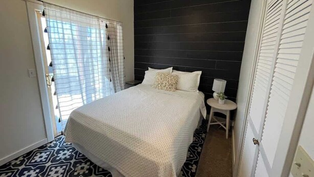 Quarto com cama, mesa de cabeceira e janela com cortinas.