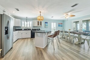 Een moderne keuken met een centraal eiland, witte kastjes en een eethoek met witte stoelen.