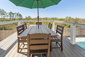 A wooden deck with a table and chairs, a green umbrella, and a view of the surrounding landscape. - Luxury Beach House, Heated Pool & Spa, Sauna, Game Room, Private Beach Access (Pensacola)