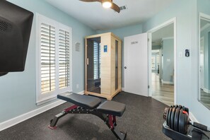 A gym with a bench, weights, and a door leading to another room. - Luxury Beach House, Heated Pool & Spa, Sauna, Game Room, Private Beach Access (Pensacola)